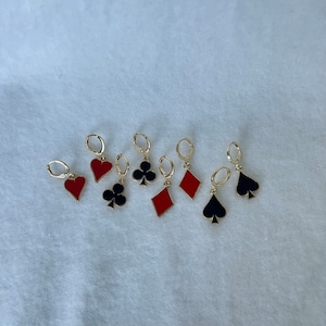May include: Six pairs of gold hoop earrings with red and black enamel charms shaped like playing card suits: hearts, clubs, diamonds, and spades.