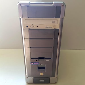 Può includere: Un case per computer a torre grigio e argento dotato di un'unità disco ottica superiore con la scritta 52x32x52x, diversi alloggiamenti per unità frontali, un piccolo logo KK blu e rosso, un pulsante di accensione centrale e un pannello inferiore con etichetta USB.