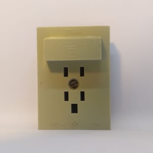 May include: A beige electrical outlet with a built-in phone jack. The outlet has three slots and is labeled "TELOS 60V= 12W".