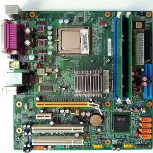 Peut inclure: Une carte mère verte Lenovo G31T-LM comprenant un socket CPU central, deux emplacements RAM avec des modules verts, un dissipateur thermique argenté, un chipset Intel, plusieurs ports d'extension et divers ports E/S arrière dont un port parallèle violet.