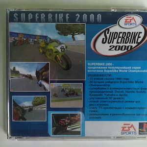 Op de afbeelding: Een blauwe en witte gamecase voor de Superbike 2000 videogame voor de Playstation-console. De case toont een foto van een motorrace en de titel van de game in grote witte letters. De achterkant van de case bevat een beschrijving van de gamefuncties in het Russisch.