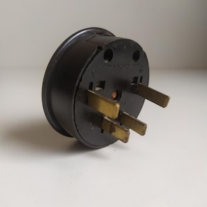 May include: A black three-prong electrical plug with gold-colored prongs.