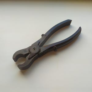 May include: A black metal wire cutter with a round handle and a spring-loaded mechanism. The cutter has a small hole in the handle.