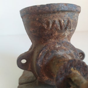 May include: A vintage cast iron coffee grinder with a worn, rusty finish. The grinder has a crank handle and a hopper for beans. The word "NWA" is visible on the side of the grinder.