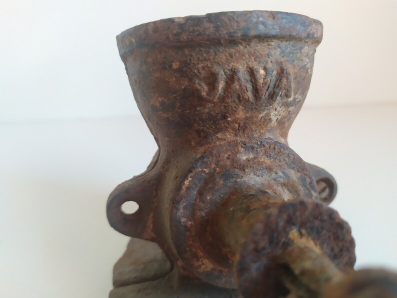 May include: A vintage cast iron coffee grinder with a worn, rusty finish. The grinder has a crank handle and a hopper for beans. The word "NWA" is visible on the side of the grinder.