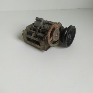 Może przedstawiać: Zbliżenie na zabytkowy, zardzewiały, metalowy tuner radiowy z czarnym plastikowym kołem zębatym. Tuner ma szereg metalowych płytek i koło zębate z zębami.