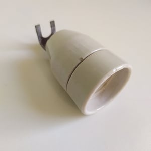 Może przedstawiać: Biały ceramiczny gniazdo żarówki z metalowym hakiem. Gniazdo jest przeznaczone do użytku ze standardowymi żarówkami.