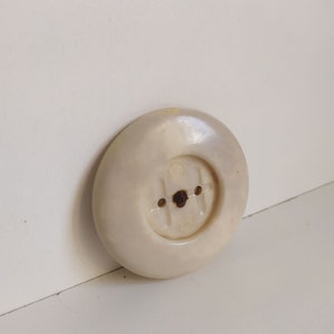 May include: A white plastic electrical outlet cover with two holes and a small metal screw in the center.