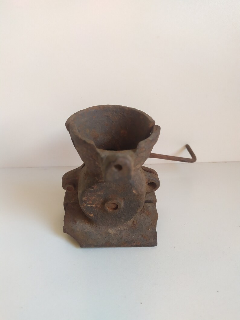 May include: A vintage cast iron hand crank grinder with a worn, rusty finish. The grinder has a small hopper and a crank handle.