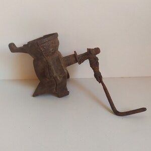 May include: A vintage cast iron corn grinder with a hand crank. The grinder is rusty and has a worn finish. The crank is made of metal and has a wooden handle.
