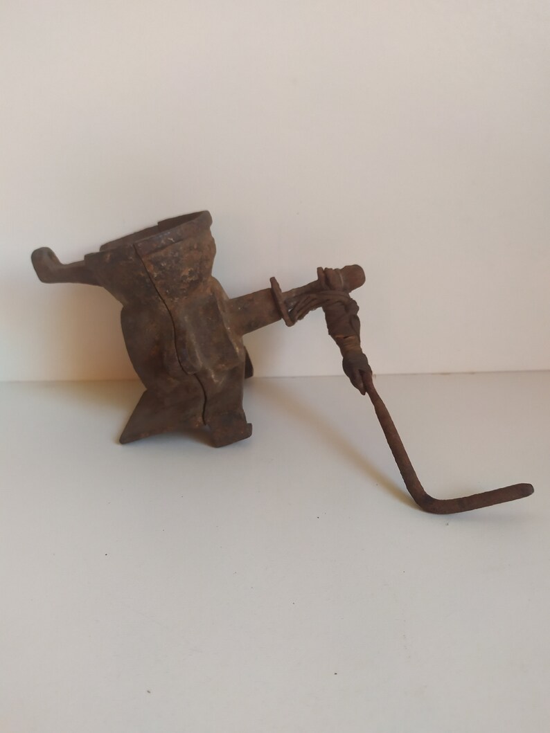 May include: A vintage cast iron corn grinder with a hand crank. The grinder is rusty and has a worn finish. The crank is made of metal and has a wooden handle.