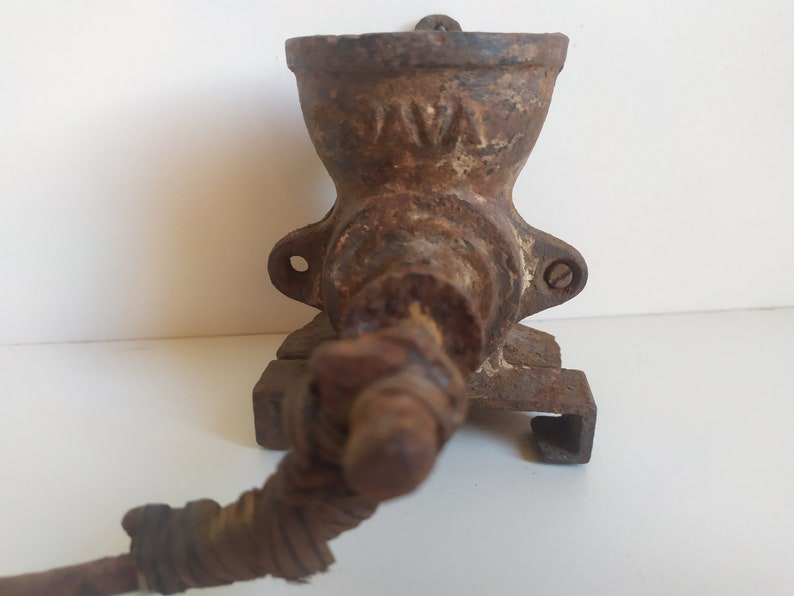 May include: A vintage cast iron coffee grinder with a hand crank. The grinder is rusty and has the word "JAVA" embossed on the side.
