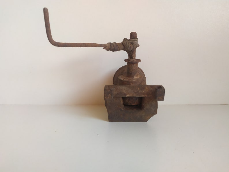 May include: A rusty metal object with a lever arm and a square base. The lever arm is wrapped with brown fabric.