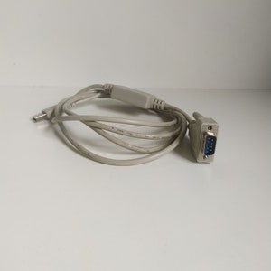 Puede incluir: Un cable adaptador USB a serie blanco con un conector macho de 9 pines en un extremo y un conector USB en el otro extremo.