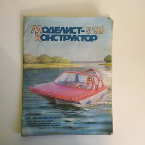 May include: A magazine cover featuring a red and white boat with a person driving it on a blue lake. The magazine cover is titled "Modelist-5'90 Konstruktor" and the text below the image reads "Amphibia! No, quasi-automobile: a boat that successfully combines excellent seafaring qualities with the comfort of a limousine. Details on page 2."