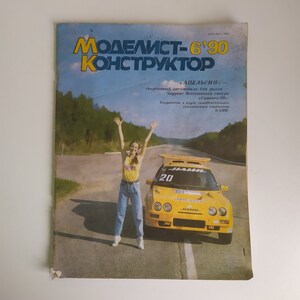 May include: A yellow sports car with the number 20 on the side, a woman in blue jeans and a yellow shirt is standing in front of the car. The car is on a road with trees in the background. The magazine cover reads "Modelist-Konstruktor 6'90" and "Apelsin".
