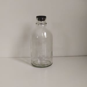 Peut inclure: Une bouteille en verre transparente avec un bouchon en plastique noir. La bouteille est vide et a une surface légèrement texturée.