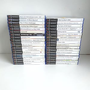以下が含まれることがあります： PlayStation 2 のビデオゲームケースが 2 つ積み重なっています。「Brian Lara International Cricket 2005」、「FIFA Football 2004」、「James Bond 007: Nightfire」、「Star Wars: Starfighter」などのタイトルがあります。ケースには青い背表紙と白いラベルが付いています。