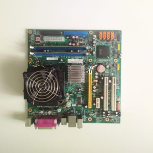 May include: A green computer motherboard with a black fan, two memory slots, and several connectors.