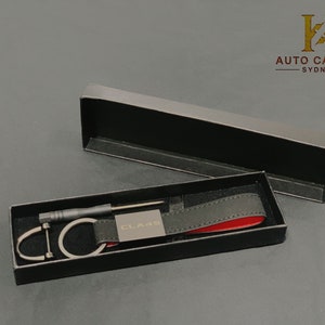 May include: A black leather key chain with a silver key ring and a small screwdriver. The keychain has a silver metal tag with the text "CLA 45" engraved on it. The keychain is in a black box with a red interior.