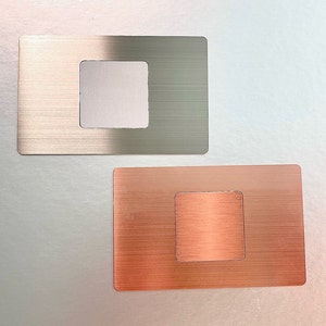 May include: Two rectangular metal plates with a square cutout in the center. The top plate is a brushed silver color, while the bottom plate is a brushed copper color.