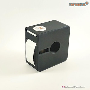 Puede incluir: Un dispensador de cinta adhesiva de plástico negro con una etiqueta blanca que dice "PRINT & LABEL" y un rollo de cinta blanca.