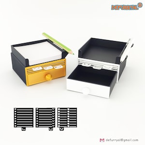 Könnte beinhalten: Zwei kleine, dekorative Schreibtisch-Organizer. Einer ist schwarz und goldfarben mit einer Schublade, einem Knopf und einem grünen Bleistift. Der andere ist schwarz und weiß mit einer Schublade und einem weißen Knopf. Die Organizer haben einen Notizblock oben drauf. Das Logo "DEFURRYAL" ist sichtbar.