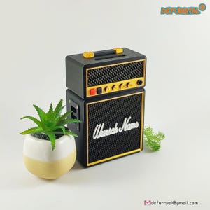 Könnte beinhalten: Schwarzer und goldener Mini-Gitarrenverstärker mit einem weißen Etikett mit der Aufschrift "Wunsch Name".