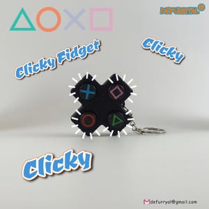 May include: A black clicky fidget keychain with four buttons shaped like the symbols from a Playstation controller. The buttons are red, blue, green, and pink. The keychain is labeled "Clicky Fidget" and "Clicky".
