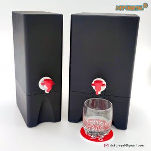 Könnte beinhalten: Zwei schwarze Getränkespender mit roten Ausgüssen und weißen Akzenten. Ein klares Glas und ein roter Untersetzer befinden sich vor einem Spender. Die Spender haben eine rechteckige Form.