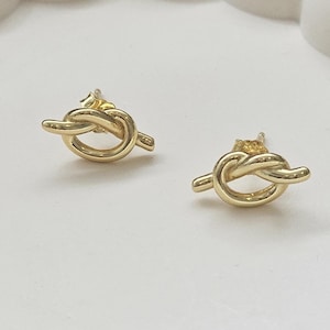 May include: A pair of gold knot-shaped stud earrings. The earrings are small and delicate, and they would make a great gift for someone special.