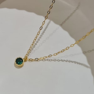 May include: A delicate gold chain necklace with a small, round, dark green gemstone pendant.
