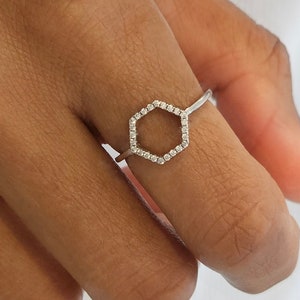 May include: A silver ring with a hexagon-shaped design. The hexagon is outlined with small, clear stones.
