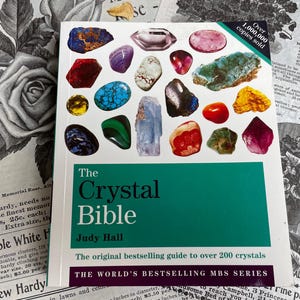 Puede incluir: El libro The Crystal Bible de Judy Hall, con una portada que muestra varios cristales coloridos. Esta guía cubre más de 200 cristales y ha vendido más de 1.000.000 de ejemplares.