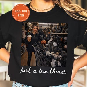 May include: A black sweatshirt featuring a graphic print of a person holding a coffee cup next to a shopping cart filled with Halloween decorations, including skulls, pumpkins, and ghosts. The text "just a few things" is printed in white below the image.