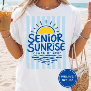 May include: White t-shirt with a blue and yellow graphic that reads "SENIOR SUNRISE CLASS OF 2027". The design includes a sun, waves, and vertical blue stripes. A round blue graphic with file type information is in the bottom right.
