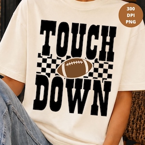 Op de afbeelding: Een crèmekleurig t-shirt met een zwarte opdruk met het woord TOUCH in grote blokletters boven een zwart-wit geblokt patroon, een bruine illustratie van een American football en het woord DOWN in grote zwarte blokletters eronder.