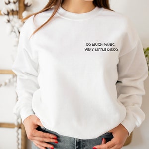 May include: White sweatshirt with the text "SO MUCH PANIC, VERY LITTLE DISCO" printed on the front.