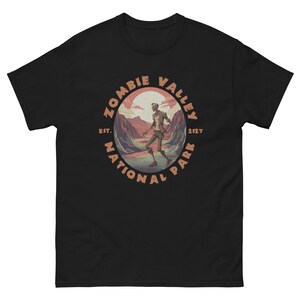 May include: Black t-shirt with a vintage-style graphic of a zombie walking through a valley. The graphic says "Zombie Valley National Park Est. 2127".