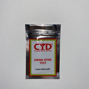 Könnte beinhalten: Ein silberner Beutel mit einem roten und gelben Etikett, auf dem "CYD Check Your Drink Drink Spike Test Is your drink safe?" steht.