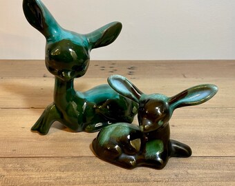 May include: Two ceramic deer figurines, one larger than the other. The larger deer is green with a light blue glaze, while the smaller deer is brown with a green glaze.