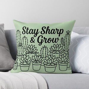 May include: A light green throw pillow with a black line drawing of cacti and succulents in pots. The pillow has the text "Stay Sharp & Grow" in a bold, black font.