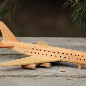 Peut inclure: Un avion en bois jouet avec une finition brun clair. L'avion a un corps long et étroit avec un nez pointu et une seule dérive. Les ailes sont légèrement balayées vers l'arrière et ont une forme arrondie. L'avion a une série de petits trous le long des côtés du corps, qui peuvent être pour la ventilation ou la décoration.