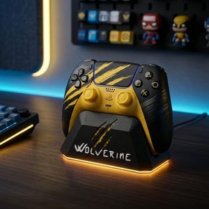 May include: A black and yellow wireless gaming controller featuring claw mark graphics, resting on a matching black charging dock with the word WOLVERINE printed in white and illuminated by a warm yellow light at the base of the stand.