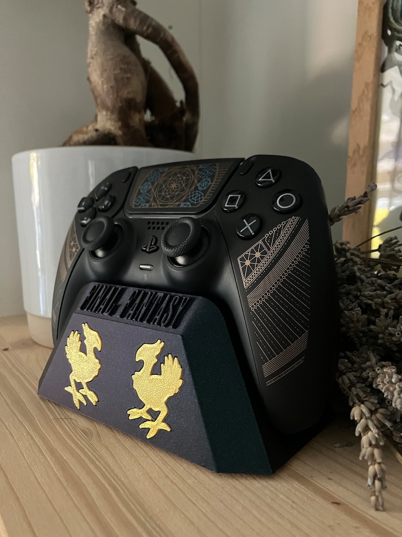 K&ouml;nnte beinhalten: Ein schwarzer PlayStation 5 DualSense-Controller mit einem goldenen Final Fantasy VII Remake-Design steht auf einem schwarzen St&auml;nder mit goldenen Final Fantasy VII Remake-Logos. Der St&auml;nder steht auf einer Holzoberfl&auml;che.