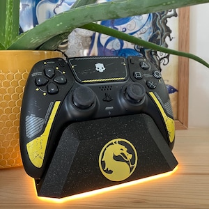 Può includere: Controller PlayStation 5 nero e giallo con base di ricarica abbinata. Il controller presenta un design a teschio e dettagli gialli. La base ha un emblema di drago dorato e una base illuminata.