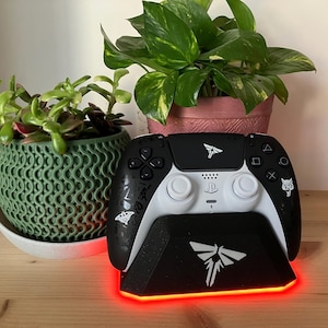 May include: A black and white video game controller with a charging stand. The stand has a red light around the base and a white firefly logo. The controller has a white firefly logo and a wolf logo.