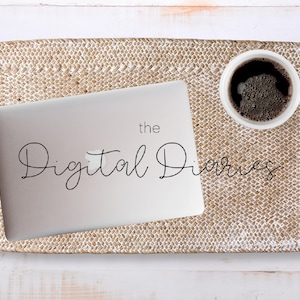 May include: A laptop computer with the text "the Digital Diaries" on the screen, sitting on a woven tray with a cup of coffee next to it.