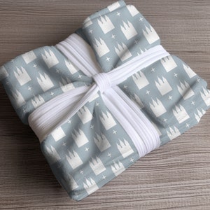 May include: A blue fabric gift wrap with a white repeating pattern of a church building and stars. The fabric is wrapped around a gift box and tied with white ribbon.