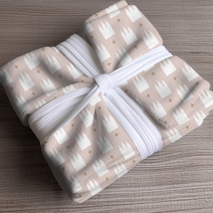 May include: A pink fabric gift wrap with a white string bow. The fabric has a repeating pattern of white church buildings and gold stars.